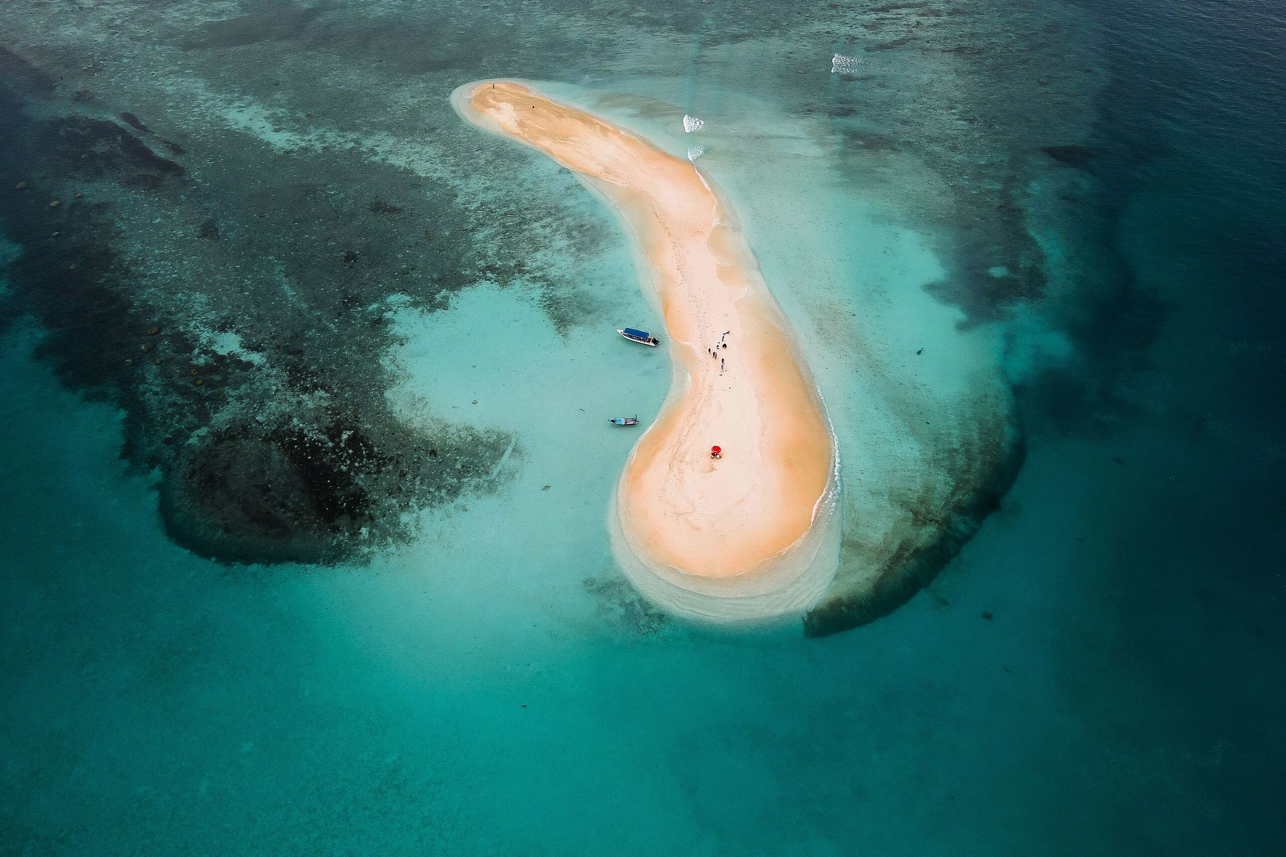 Aerial view of a curved sandbank island surrounded by turquoise reef