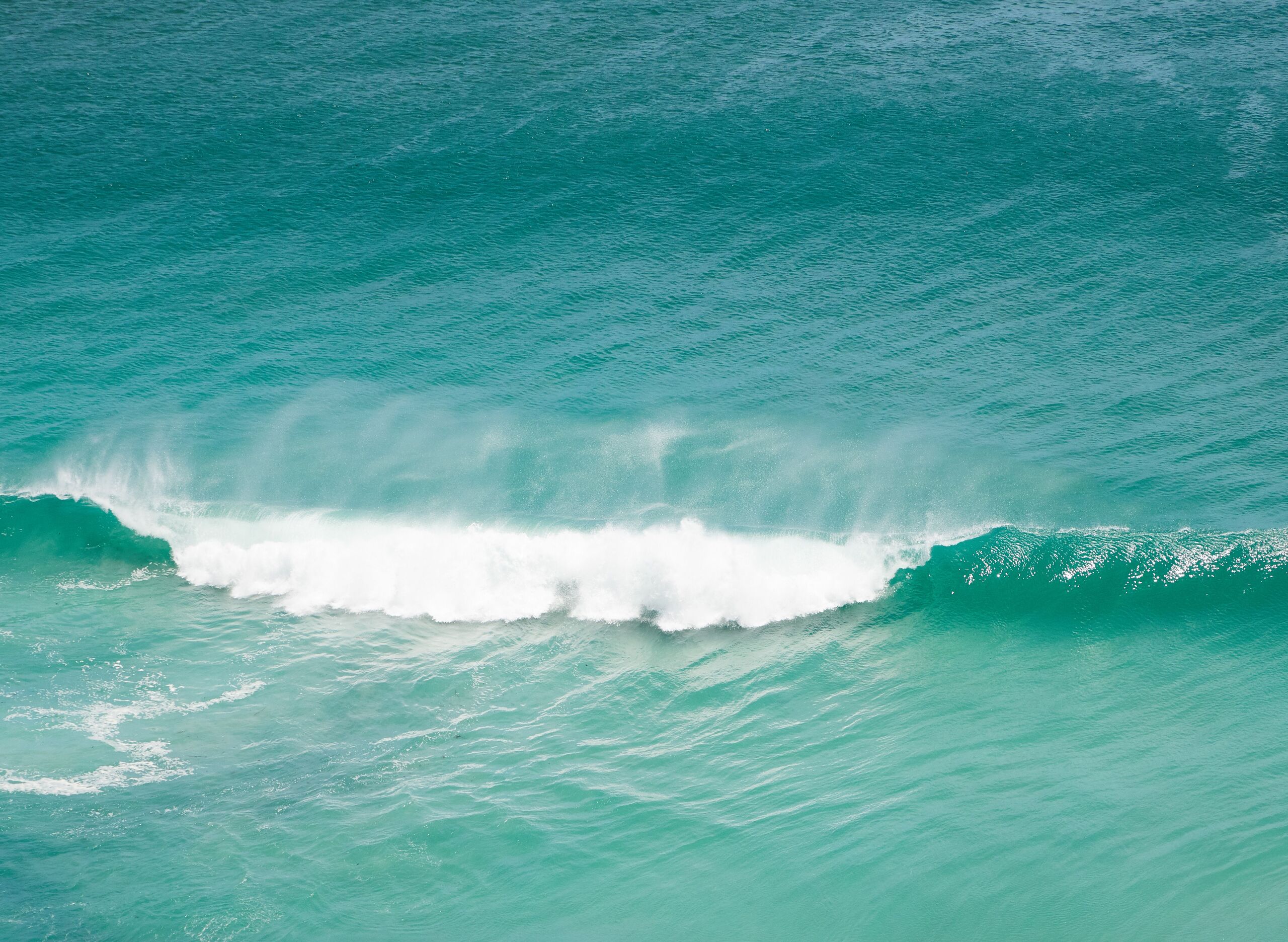 A turquoise wave peeling across the open Pacific, seen from above