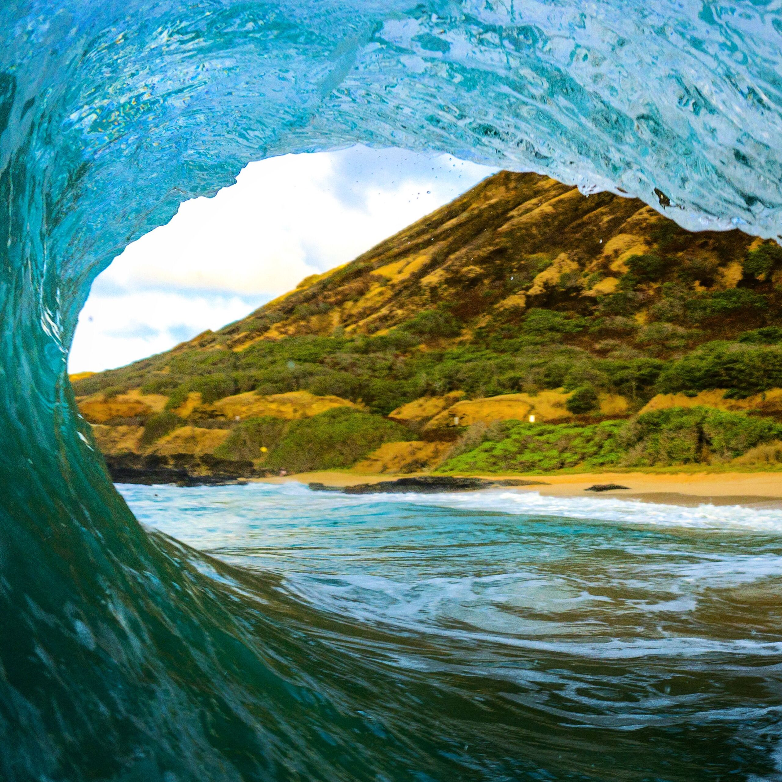View from inside a breaking wave toward sunlit island hills